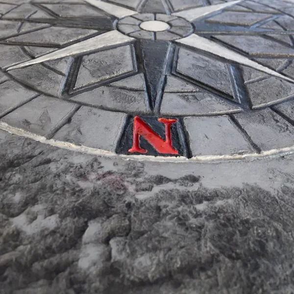 Close detail of a decorative concrete compass rose inlay showing the red north point