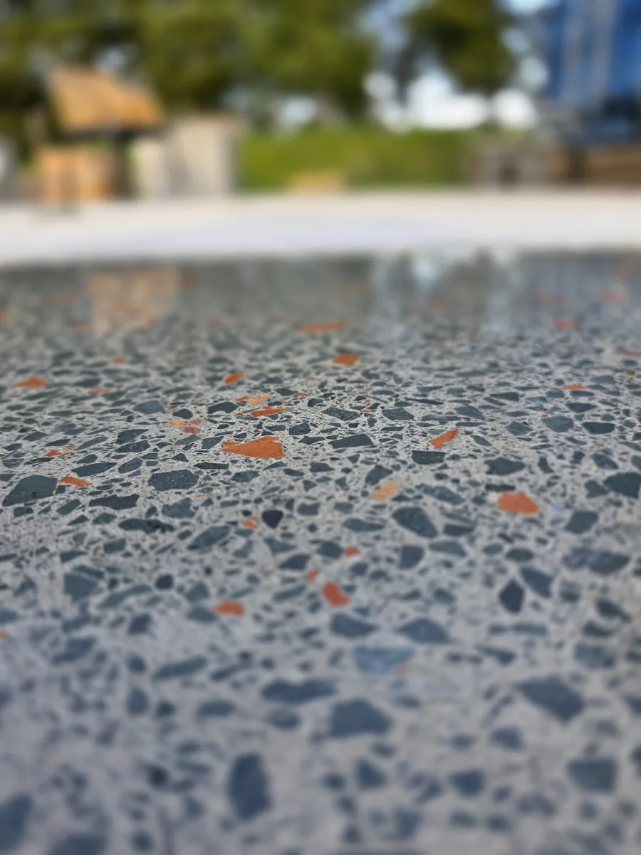 Full aggregate exposure: a dense terrazzo-like reveal of blue-grey stone and terracotta brick aggregate in polished concrete