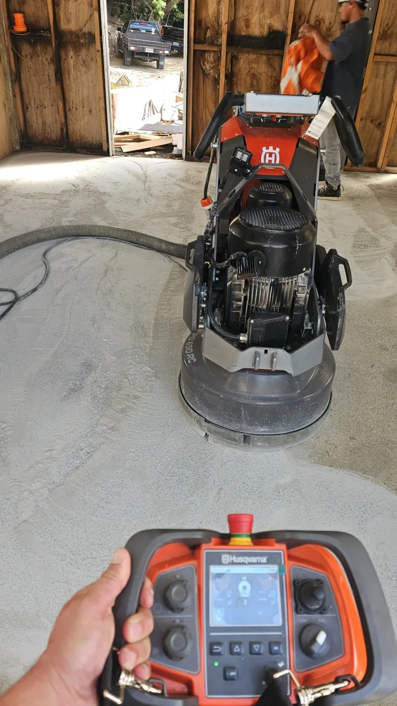 Remote-controlled Husqvarna planetary grinder with handheld controller polishing a concrete floor under dust extraction